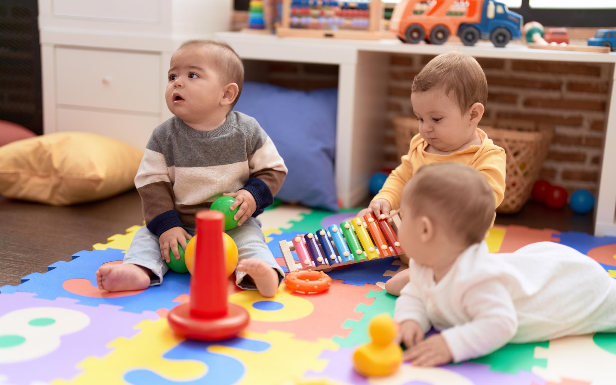 Drei Babys sitzen auf dem Boden und spielen mit Spielzeug